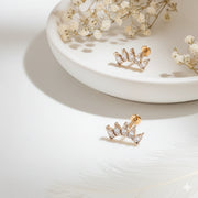 Two 14k rose gold white sapphire crescent cartilage studs displayed on ceramic tray with dried flowers