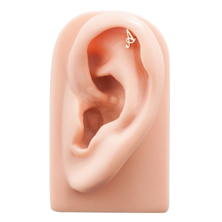 14K gold letter A flat back stud shown in helix piercing on silicone ear model for placement reference