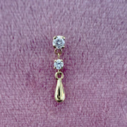 14K yellow gold dew drop labret stud with dual CZ stones, shown on textured surface for scale