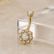 Gold belly button ring with diamond accents on a beige background