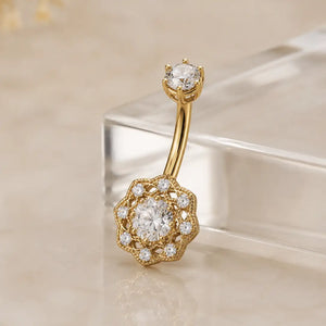 Gold belly button ring with diamond accents on a beige background