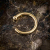 Close-up of 18K yellow gold nose hoop on dark stone surface showing ball-end detail and polish