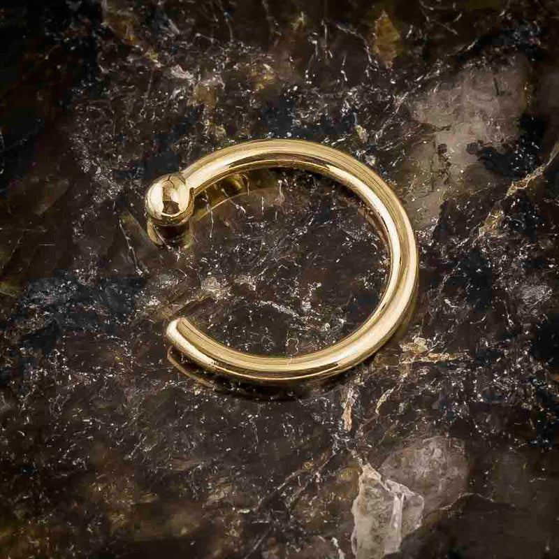 Close-up of 18K yellow gold nose hoop on dark stone surface showing ball-end detail and polish