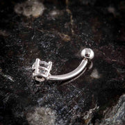 Side profile of 14k white gold diamond navel ring showing curved barbell and prong setting on dark stone surface