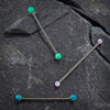 Three opal industrial barbells in teal and pink laid on dark stone surface showing full barbell length