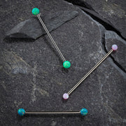 Three opal industrial barbells on dark stone showing green, pink, and teal opal color options