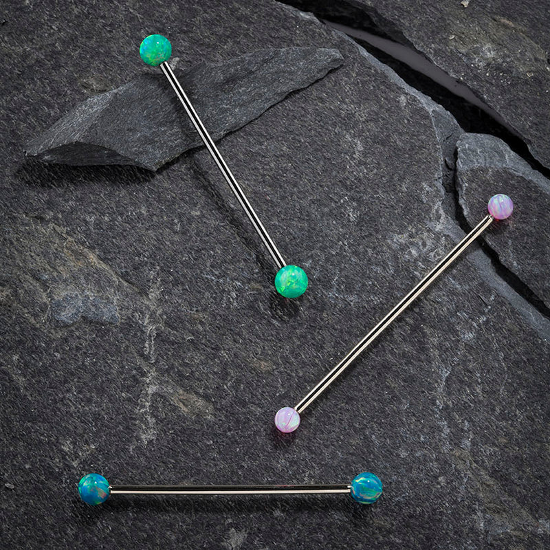 Three opal industrial barbells on dark stone showing green, pink, and teal opal color options