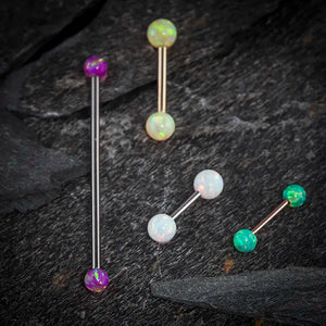 Assorted opal industrial barbells in purple, white, and green on dark stone surface showing color variety