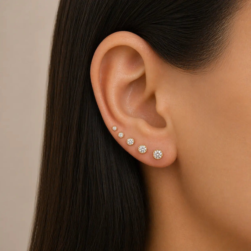Close-up of an ear wearing multiple diamond stud earrings on a neutral background