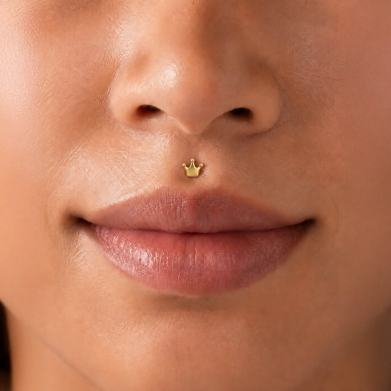Model close-up of an woman's nose with a solid gold crown flat back labret stud in her medusa piercing.