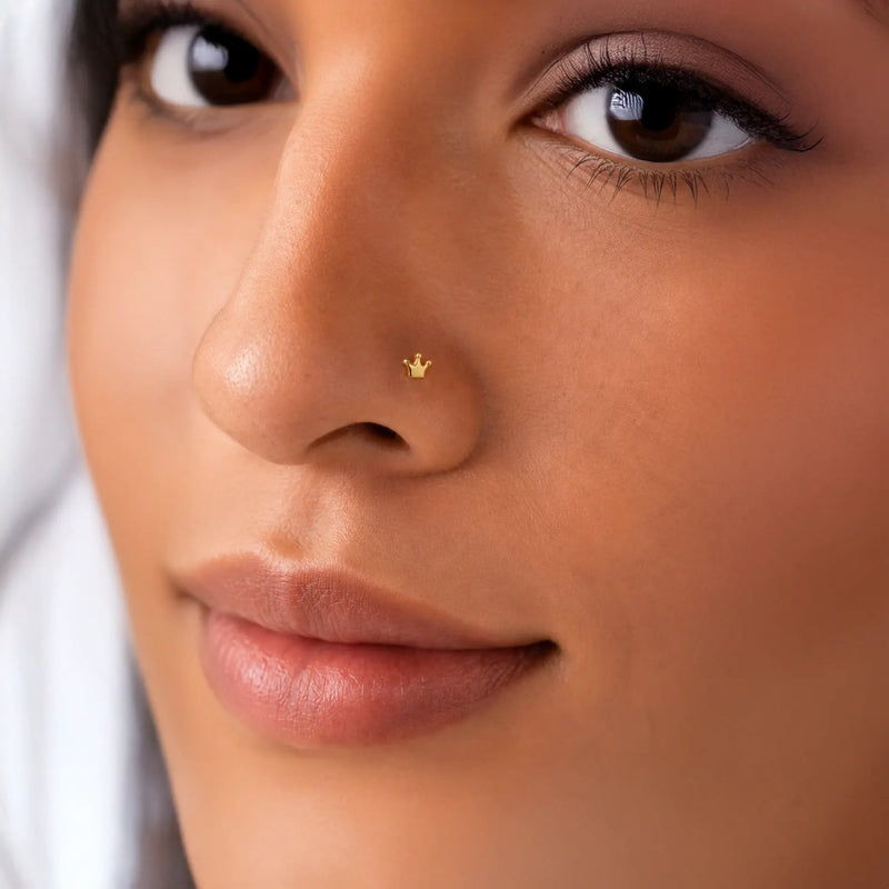 Close-up of a woman's face wearing a 14k gold crown stud nose ring with a white background