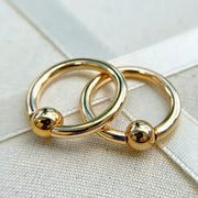 Two 14K yellow gold fixed bead rings overlapping on linen surface, showing size variation