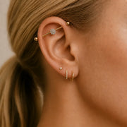 Close-up of an ear with gold earrings and Jasmine industrial barbell against a neutral background