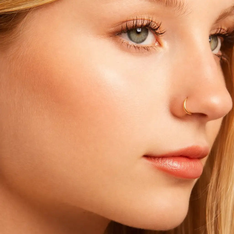 18K yellow gold plain clicker hoop worn as nose ring on model, close-up side profile view