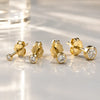 Four 14K yellow gold bezel-set diamond studs in graduated sizes arranged on a reflective surface