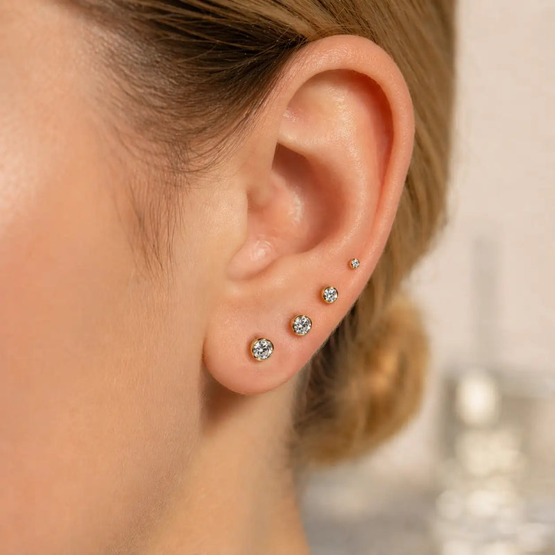 14K gold bezel-set diamond studs in multiple sizes styled as an ear stack on a model