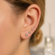 Four bezel-set diamond stud earrings in graduating sizes worn in multiple ear piercings on a model