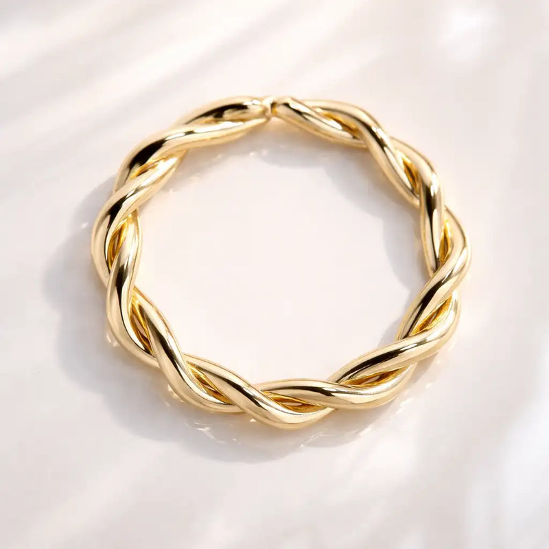 14K yellow gold twisted seamless ring on white marble surface, highlighting polished braid texture