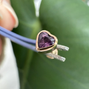 Close-up of 14k rose gold amethyst heart earring held by tweezers, showing post and bezel detail