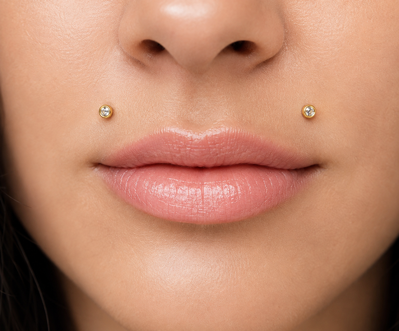 Angel bites piercing with a pair of gold bezel-set studs, one either side of the upper lip
