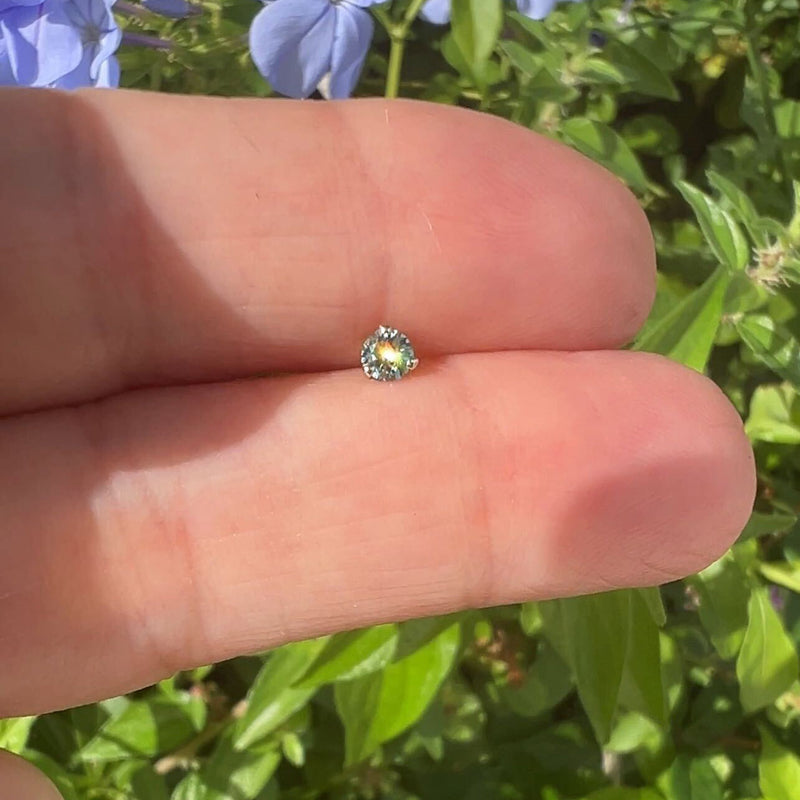 Loose 2.5mm aqua diamond resting on fingertip in natural sunlight showing color and sparkle