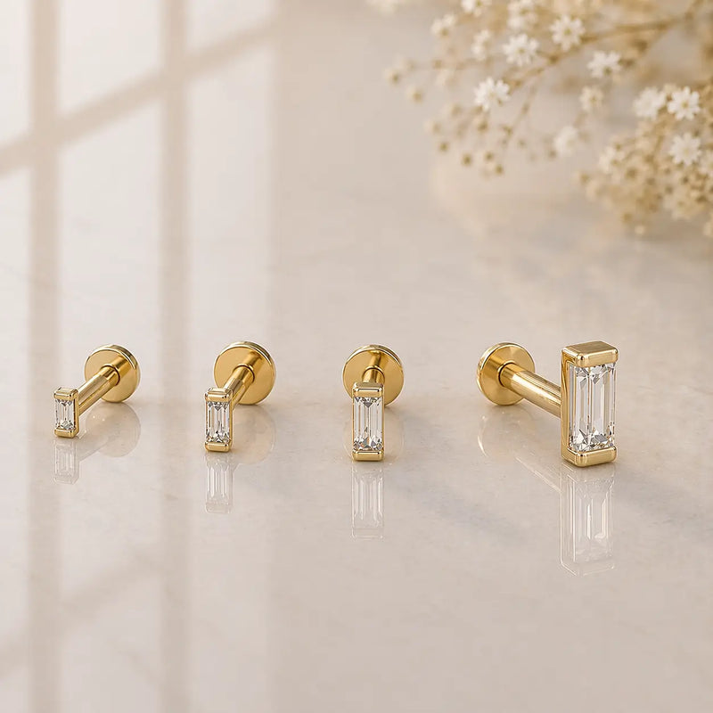All four sizes of 14k yellow gold baguette diamond flat back studs displayed on marble surface