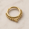 Gold seam ring septum piercing jewelry with bead detailing on a beige background