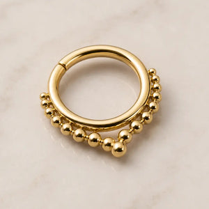 Gold seam ring septum piercing jewelry with bead detailing on a beige background