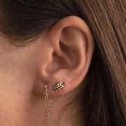 14k gold olive branch piercing stud shown on model's earlobe piercing, styled with chain earring