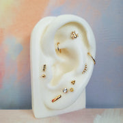 Gold bee cartilage stud styled on a white ear mannequin in a curated multi-piercing flat lay