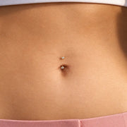 Close-up of a model's belly button piercing with a 3mm bezel-set curved barbell - two small clear stones set in 14k yellow gold