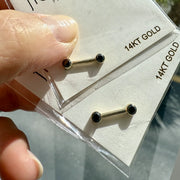 Two 14K yellow gold black diamond nipple barbells held in hand on FreshTrends packaging for scale