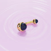 14k yellow gold black Akoya pearl navel ring laid flat on pink rippled surface, lifestyle shot