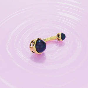 14k yellow gold black Akoya pearl navel ring laid flat on pink rippled surface, lifestyle shot