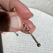 14k gold bow industrial barbell held between fingers to show size, scale, and bow detail up close