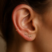 14k gold mini bow flat back studs worn in two lobe piercings, styled with a gold ear cuff