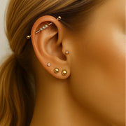 Gold bubble cabochon industrial barbell shown in ear piercing alongside stacked gold earrings