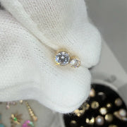 Gold earring with a large central diamond and smaller side stone on a white fabric background.