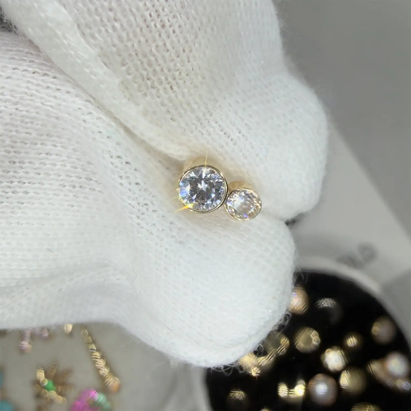 Gold earring with a large central diamond and smaller side stone on a white fabric background.