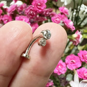 14k white gold CZ bubble bezel floating navel ring held on fingertip with floral background for scale