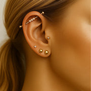 14k gold bubble gem industrial barbell shown in ear piercing, styled with multiple gold ear piercings