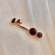 14k rose gold garnet bubble bezel navel ring laid flat on fabric, angled view