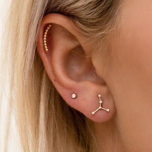 14k gold Taurus constellation flat back earring worn in lobe piercing, close-up on ear