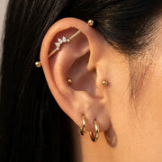 Close-up of a person's ear adorned with multiple gold ear piercings, including hoop earrings, small studs, a helix stud, and the Celeste Arc industrial barbell.