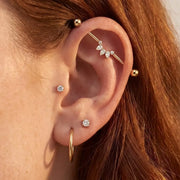 Close-up of a person's ear adorned with multiple gold ear piercings, including hoop earrings, small studs, a helix stud, and the Celeste Arc industrial barbell.