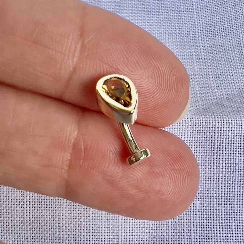 Citrine teardrop floating navel ring in 14k gold held between fingers for size reference