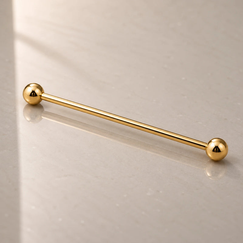 A gold industrial barbell with ball ends, resting diagonally on a light gray reflective surface.