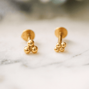 Pair of 14k yellow gold trinity bead flat back studs displayed front and side view on marble surface