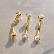 14k yellow gold curved barbells styled alongside CZ and pearl end variations on marble surface