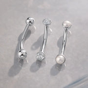 14k white gold curved barbells displayed with CZ bezel and pearl end styles on gray surface